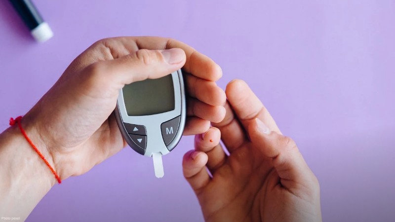 Hands holding a glucometer to test blood sugar levels on a purple background., tags: approval glucose monitor - pexel