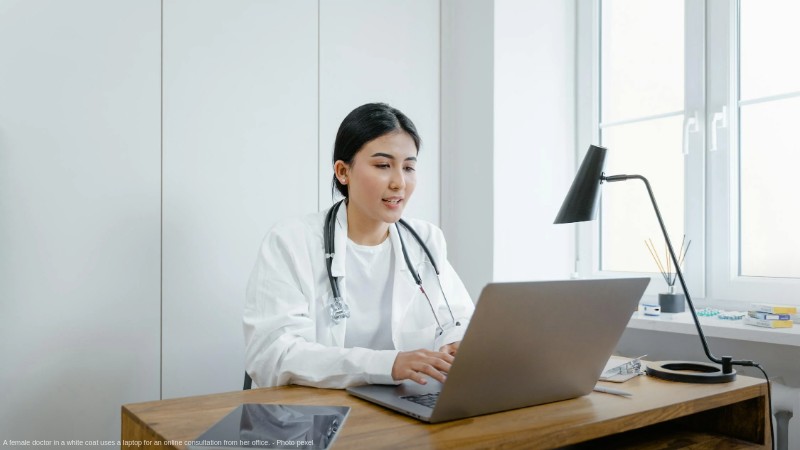 A female doctor in a white coat uses a laptop for an online consultation from her office., tags: medicare extends - pexel