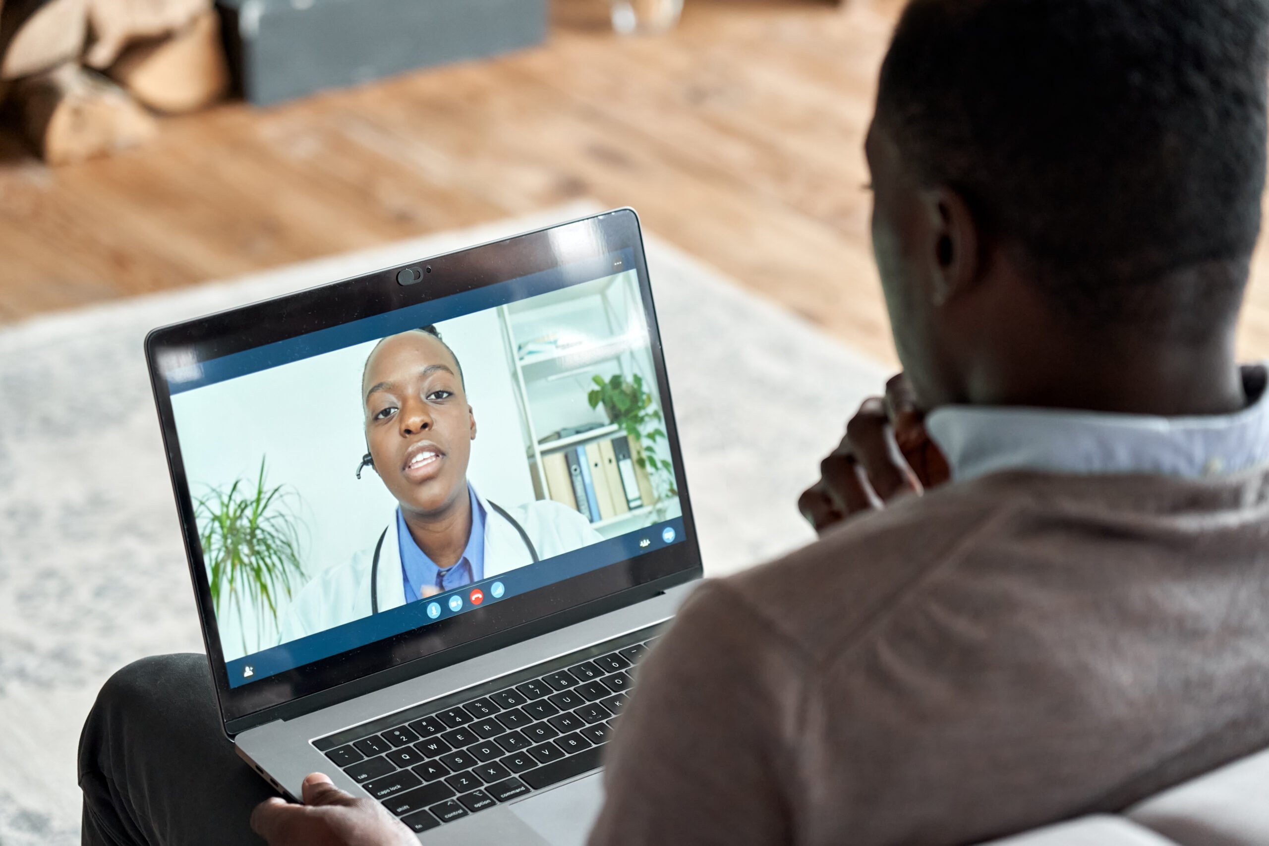 Man talking to female doctor on his computer while relaxing in his living room
